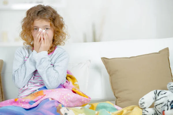 Ung flicka satt på soffan, blåser näsan — Stockfoto