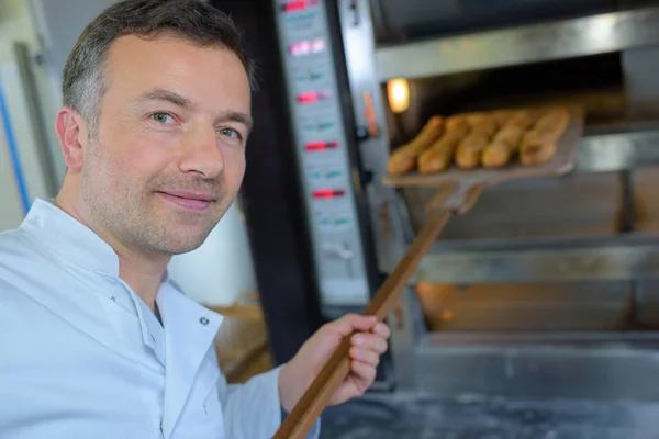 Baker getting fresh bread out of the traditional oven — Stock Photo, Image
