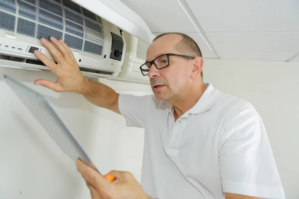 Homem usando um tablet para ajustar o sistema de ar condicionado — Fotografia de Stock