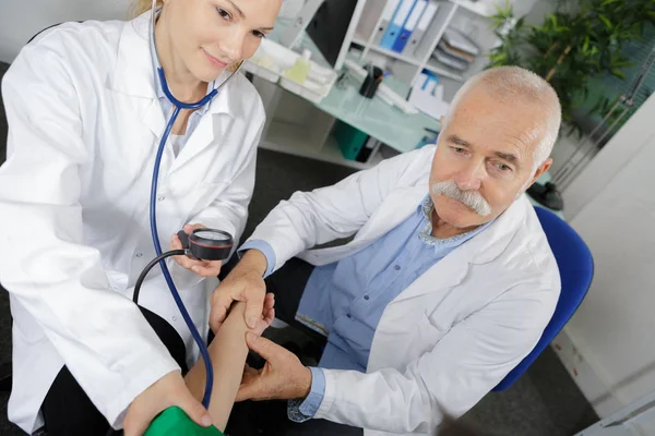 Médico internista feminino tomando pacientes pressão arterial sob vigilância — Fotografia de Stock