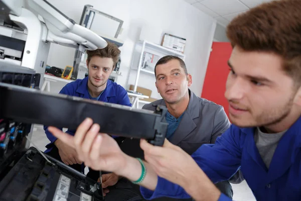 Jonge technicus bezig met fotokopieerapparaat wordt begeleid door collega 's — Stockfoto