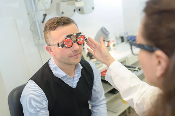 Optometrista joven feliz haciendo pruebas de visión para pacientes masculinos — Foto de Stock