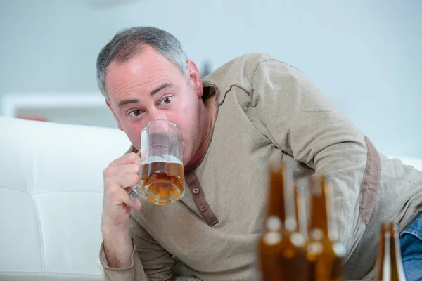 Mature drunk man drinks a beer on the sofa — Stock Photo, Image