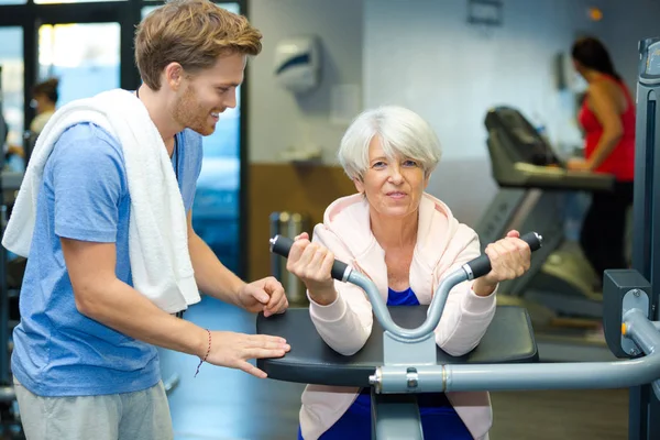 Seniorin im Fitnessstudio vom Trainer unterstützt — Stockfoto