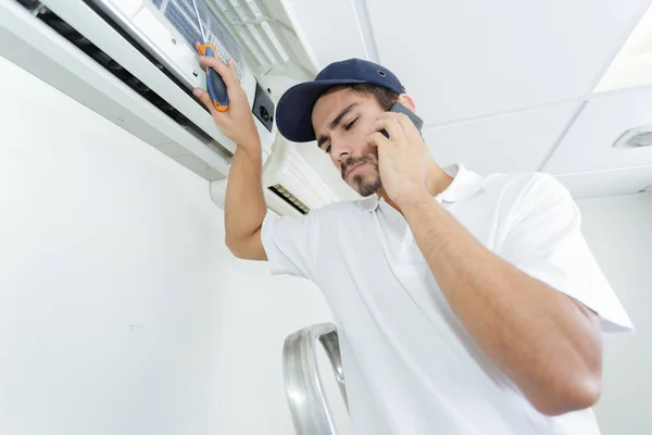 Joven manitas reparando el sistema de aire acondicionado pidiendo ayuda —  Fotos de Stock