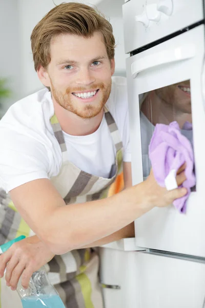Krásný usměvavý mladý muž čištění trouby — Stock fotografie