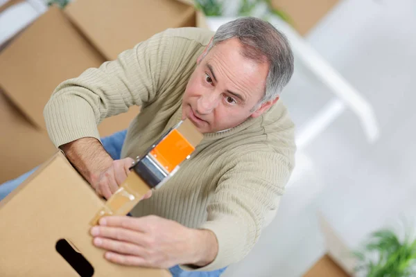 Homem que embala uma caixa móvel usando uma fita adesiva — Fotografia de Stock