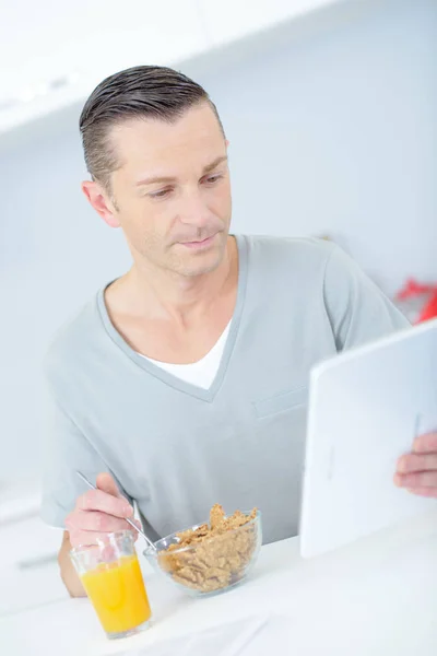 Mann liest beim Frühstück Nachrichten auf dem Tablet — Stockfoto