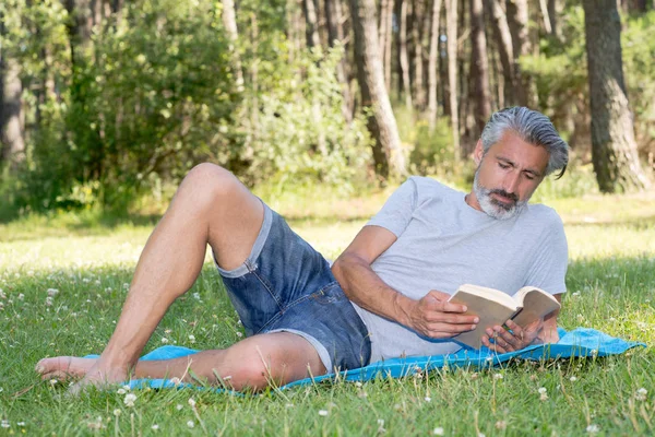 Adam lyingsitting bir kitap okuma çim — Stok fotoğraf