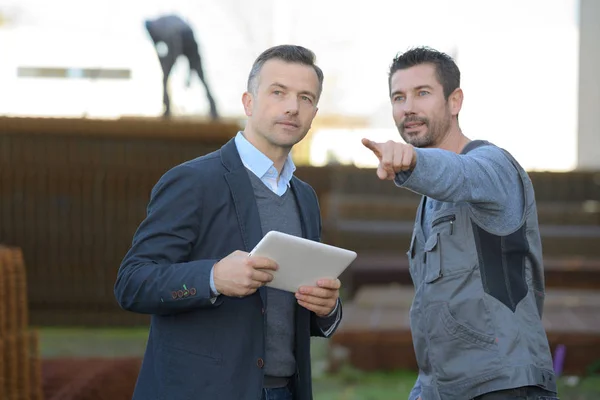 Engineer with digital tablet pointing away outside industry — Stock Photo, Image