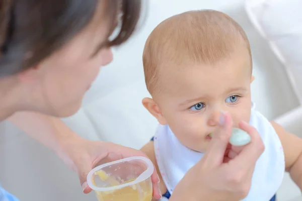 Женщина кормит ребенка ложкой из пластикового горшка с едой — стоковое фото