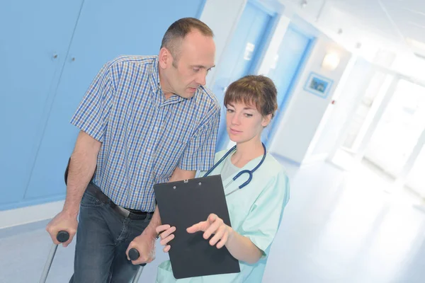 Mannelijke patiënt met cast en verpleegkundige in ziekenhuis gang — Stockfoto