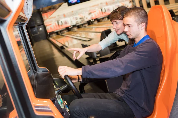 Young couple playing driving wheel video game in game room — Stock Photo, Image