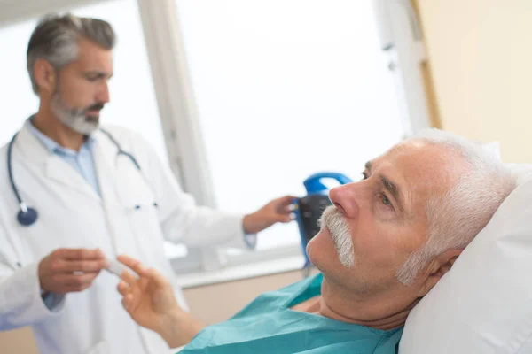 Arzt mit krankem alten Mann liegt im Krankenhausbett — Stockfoto