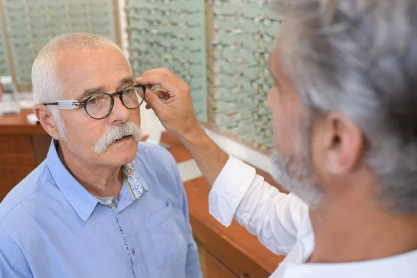 Senior man probeert bril frames aan opticien — Stockfoto