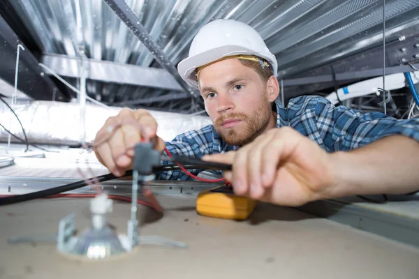 Ung man elektriker ledningar inne i taket — Stockfoto