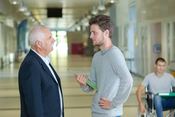 Professor met notebook in gesprek met een student in de gang — Stockfoto