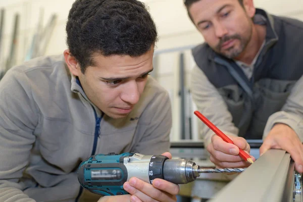 Arbeiter bohrt Loch als Kollege Position markiert — Stockfoto