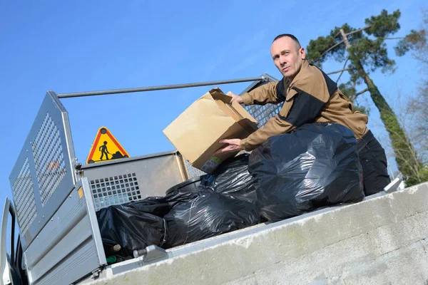 Man amidst refuse bags in pickup truck