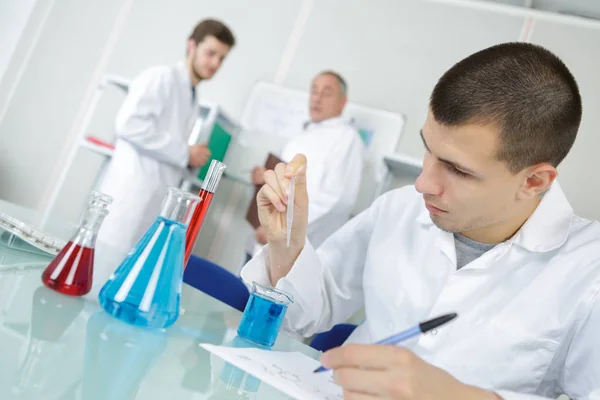 Чоловіча медична лабораторія молодий дослідник проводить тести з синьою рідиною — стокове фото