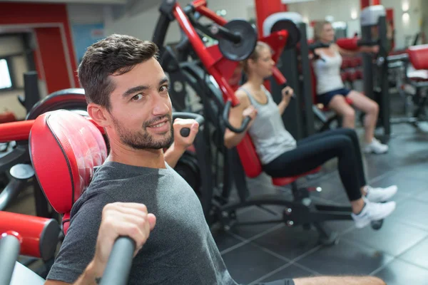 Jovem adulto fazendo powerlifting em máquinas no clube de fitness — Fotografia de Stock