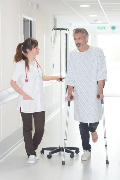 Female doctor talking to male patient with crutches in hospital-corridor — Stock Photo, Image