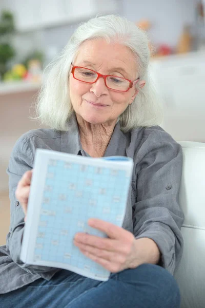 Starsza kobieta robi krzyżówka — Zdjęcie stockowe