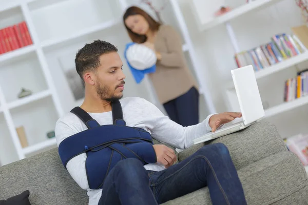 Man with arm sling support using laptop — Stock Photo, Image