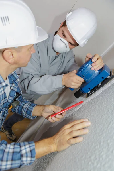 Apprentice builder sanding interior wall for restoration — Stock Photo, Image