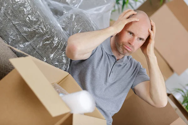 Hombre frustrado sentado entre cajas de cartón marrón —  Fotos de Stock