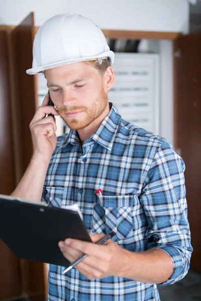 Ingeniero de construcción ocupado hablando por teléfono y sujetando el portapapeles —  Fotos de Stock