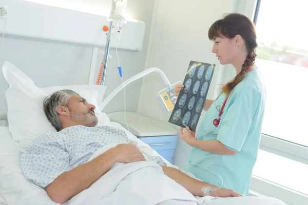 A doctor showing an x-ray to a patient on bed — Stock Photo, Image