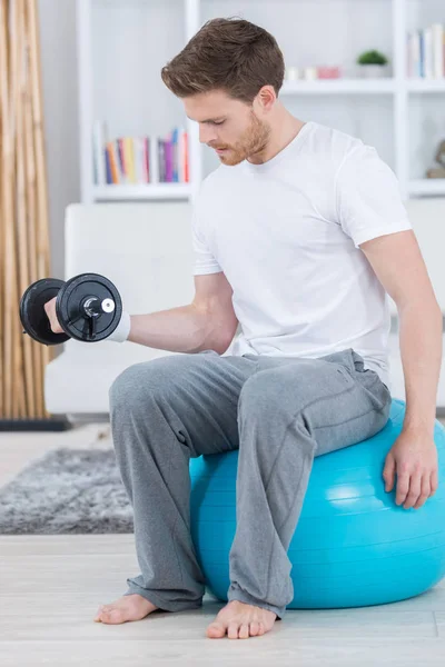 Attraktiver junger Mann mit Schweizer Ball, der zu Hause Übungen macht — Stockfoto