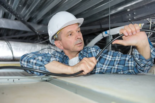 屋根のスペースにケーブルを曲げ電気技師 — ストック写真