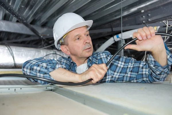 Elektriker bockning kabel i tak utrymmet — Stockfoto