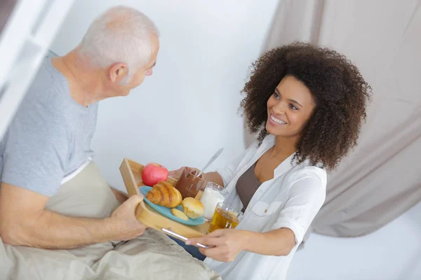 Kvinnlig sjuksköterska hålla en bricka med frukost för senior — Stockfoto