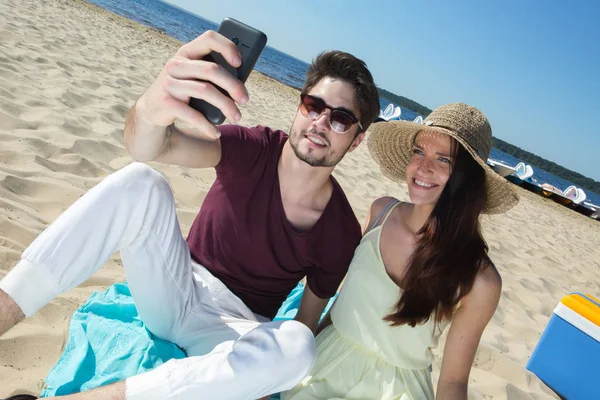 Lindo jovem casal sentado na praia e fazendo selfie — Fotografia de Stock