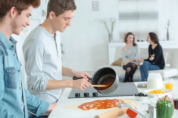 Jonge mannen maken pizza, vriendinnen zat op de Bank — Stockfoto