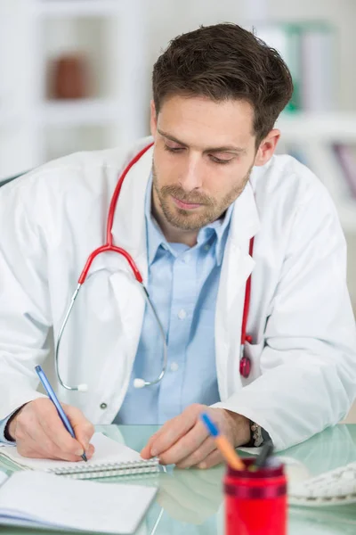 Um médico do sexo masculino escrevendo prescrição na mesa — Fotografia de Stock