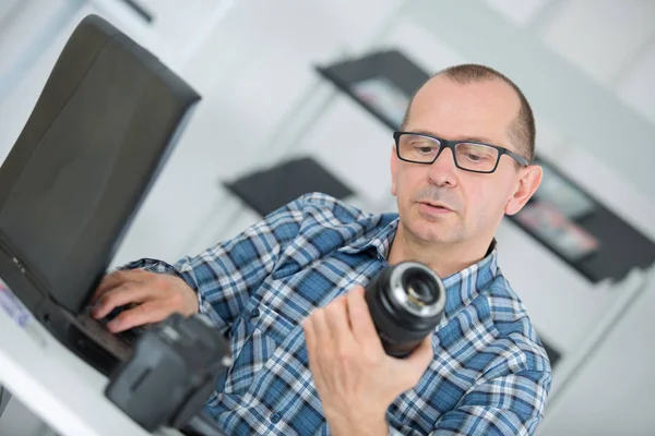 Bir kamera tutarak ve dizüstü bilgisayarda yazarak adam — Stok fotoğraf