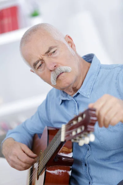 Ανώτερος άνθρωπος στο σπίτι μαθαίνει να παίζει κιθάρα — Φωτογραφία Αρχείου