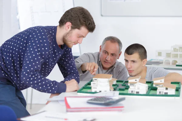 Arquitectos con modelo de casa y planos trabajando en oficina — Foto de Stock