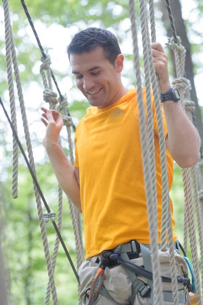 Bello felice giovane uomo attraversare ponte di corda — Foto Stock