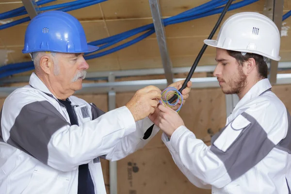 Elettricista con apprendista che lavora in una nuova casa — Foto Stock