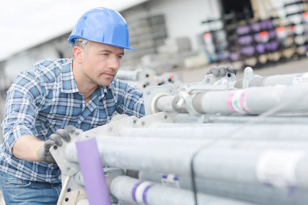 Arbeiter schiebt Stapel von Gerüststangen — Stockfoto