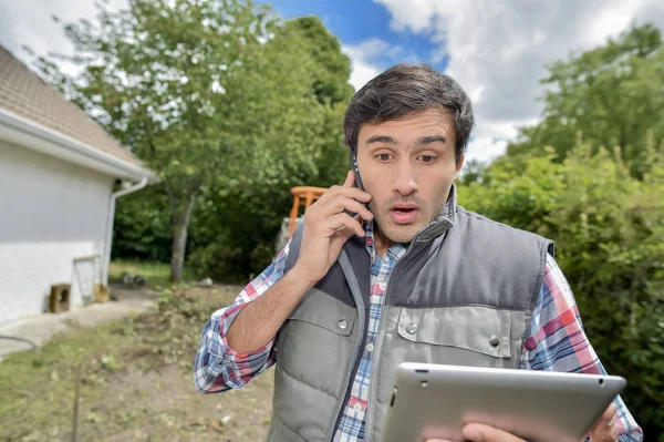 Férfi keresi a tablettát, telefon, hogy a fülébe, háztáji sokkolta kifejezés — Stock Fotó