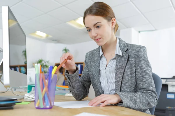 Jonge vrouwelijke beambte bij computerbureau sorteren potloden — Stockfoto