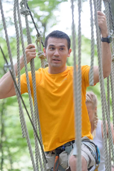 Hombre guapo cruzando un puente de cuerda — Foto de Stock