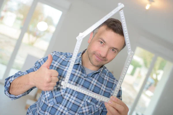 Portrait of man looking through ruler folded into a house shape — Stock Photo, Image