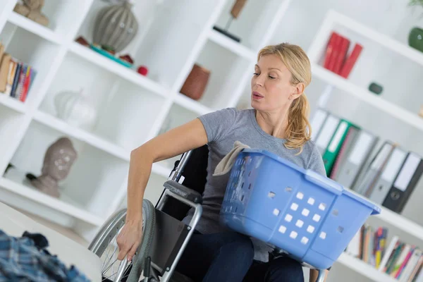 Woman on wheelchair carrying basket of laundry around home — Stock Photo, Image